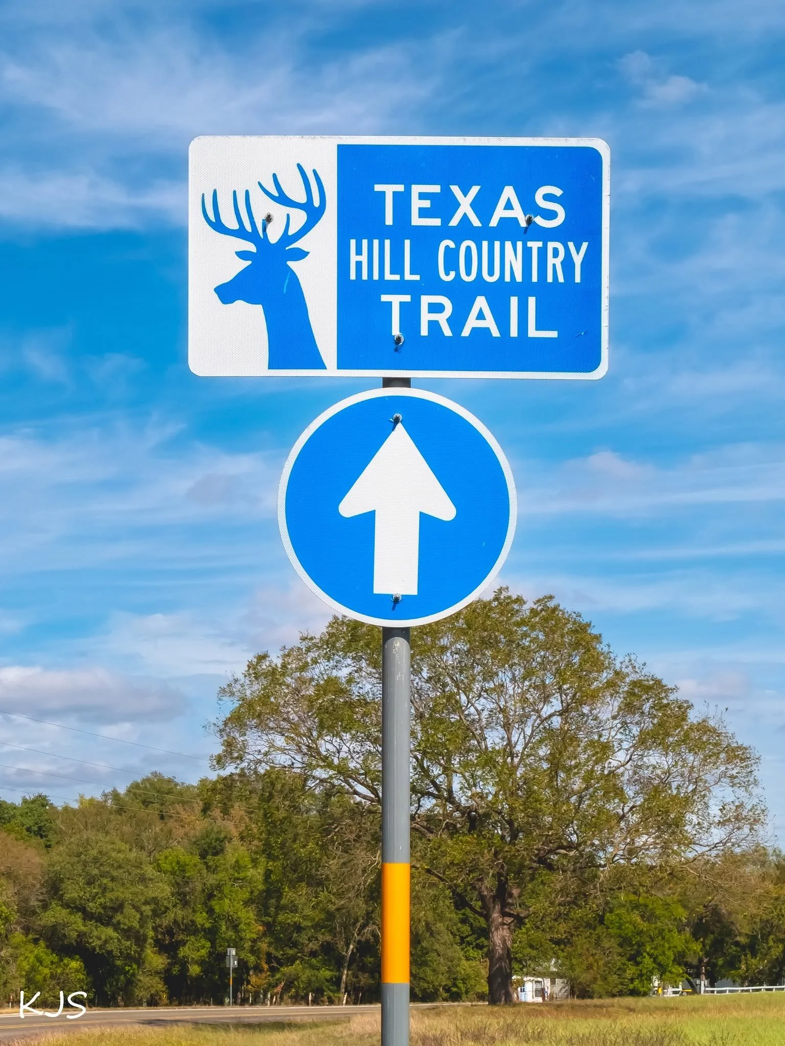 A blue and white sign indicating the Texas Hill Country Trail with a deer head silhouette and an upward arrow below.