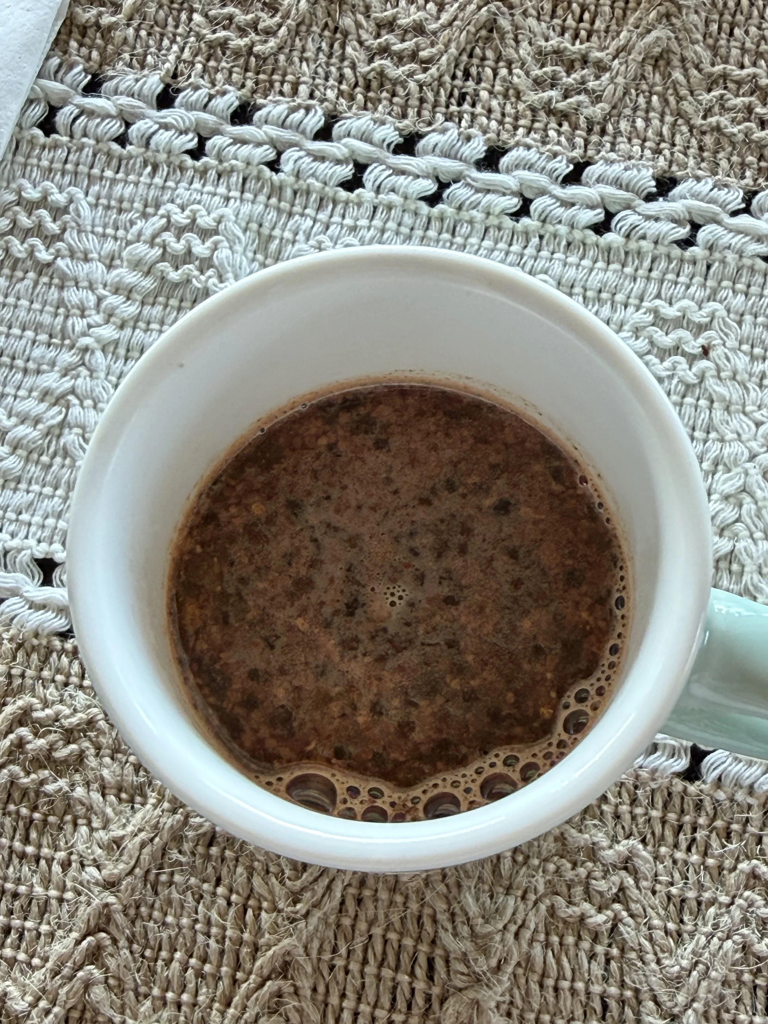 A white coffee mug filled with hot chocolate topped with marshmallows, placed on a textured woven mat.
