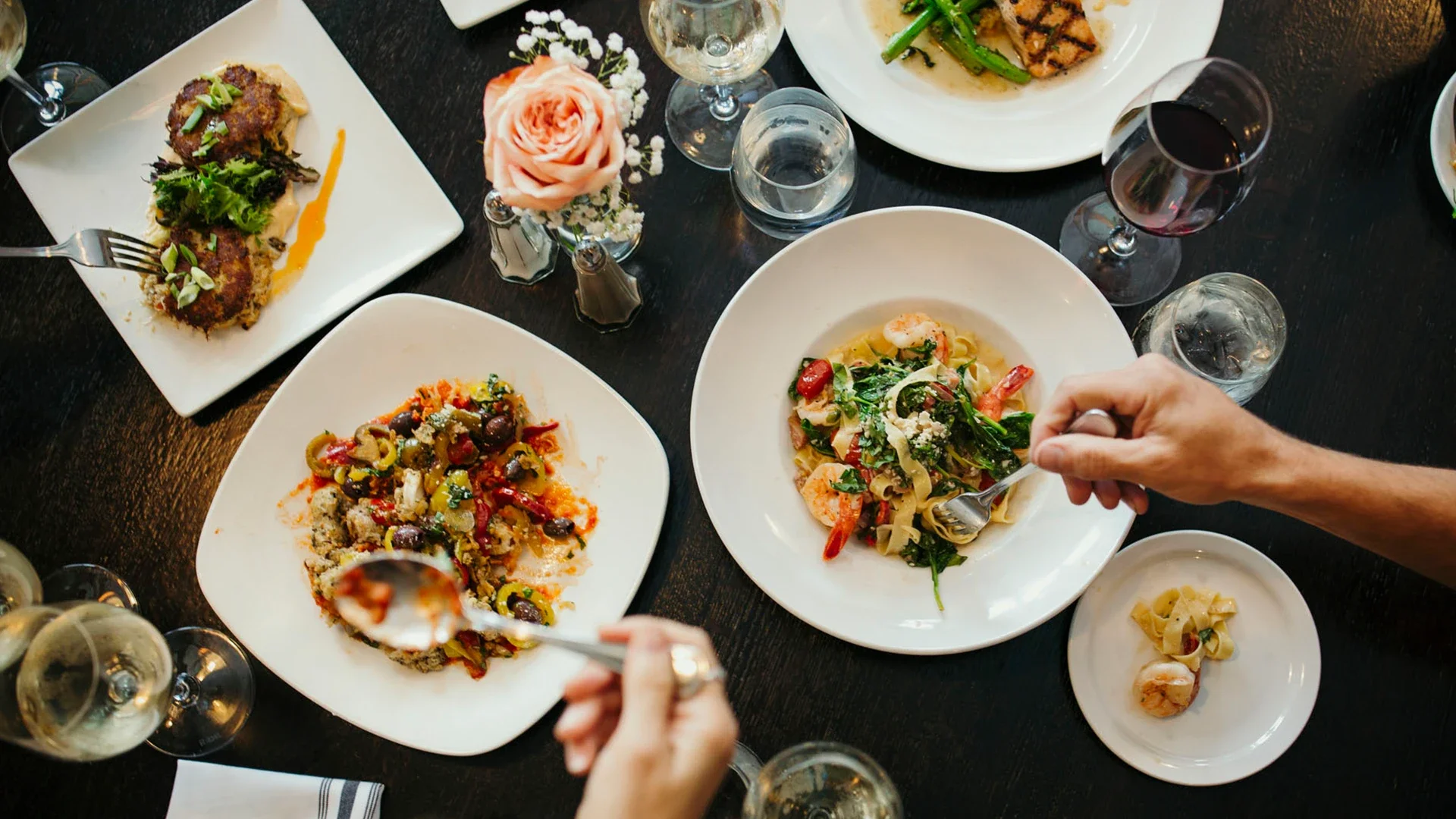 A dinner table at Warfield's restaurant in Clifton Springs, NY, with various plates of pasta, a salad, a meat dish, and glasses of red and white wine. A person is serving themselves pasta.