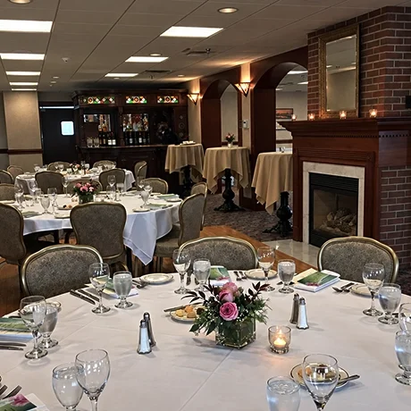Elegant dining room set up at Warfield's restaurant in Clifton Springs, NY, with round tables covered in white tablecloths, each with water glasses, plates, silverware, and floral centrepieces, in front of a brick fireplace.