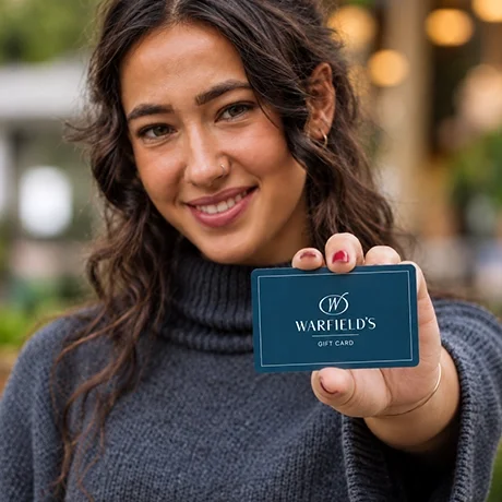 Young woman smiling and holding a Warfield's restaurant gift card outdoors.