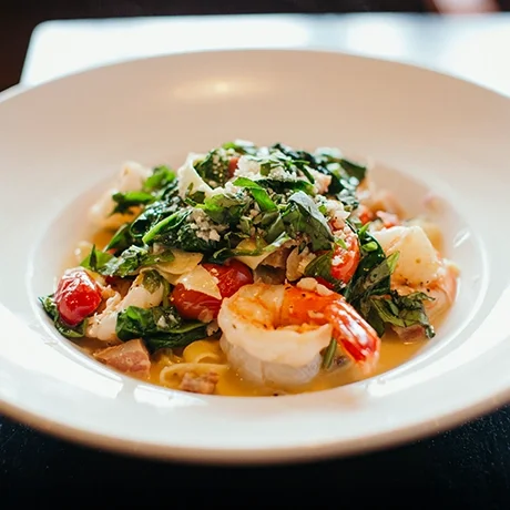 Seafood pasta with shrimp, cherry tomatoes, spinach, and grated cheese in a white bowl.