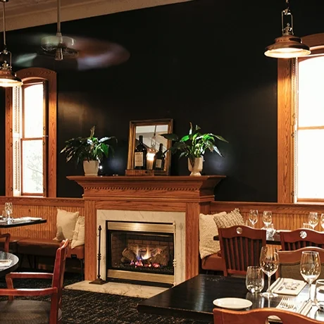Cozy restaurant interior with a fireplace, wooden furniture, and potted plants on the mantle at Warfield's restaurant in Clifton Springs, NY.