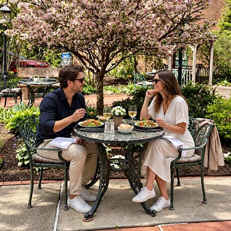 A man and a woman are sitting at a table outside Warfield's restaurant in Clifton Springs, NY, enjoying a meal under a blooming cherry blossom tree with greenery and a sidewalk in the background.