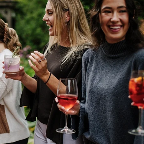 Two women smiling and holding wine glasses at an outdoor gathering at Warfield's restaurant in Clifton Springs, NY.