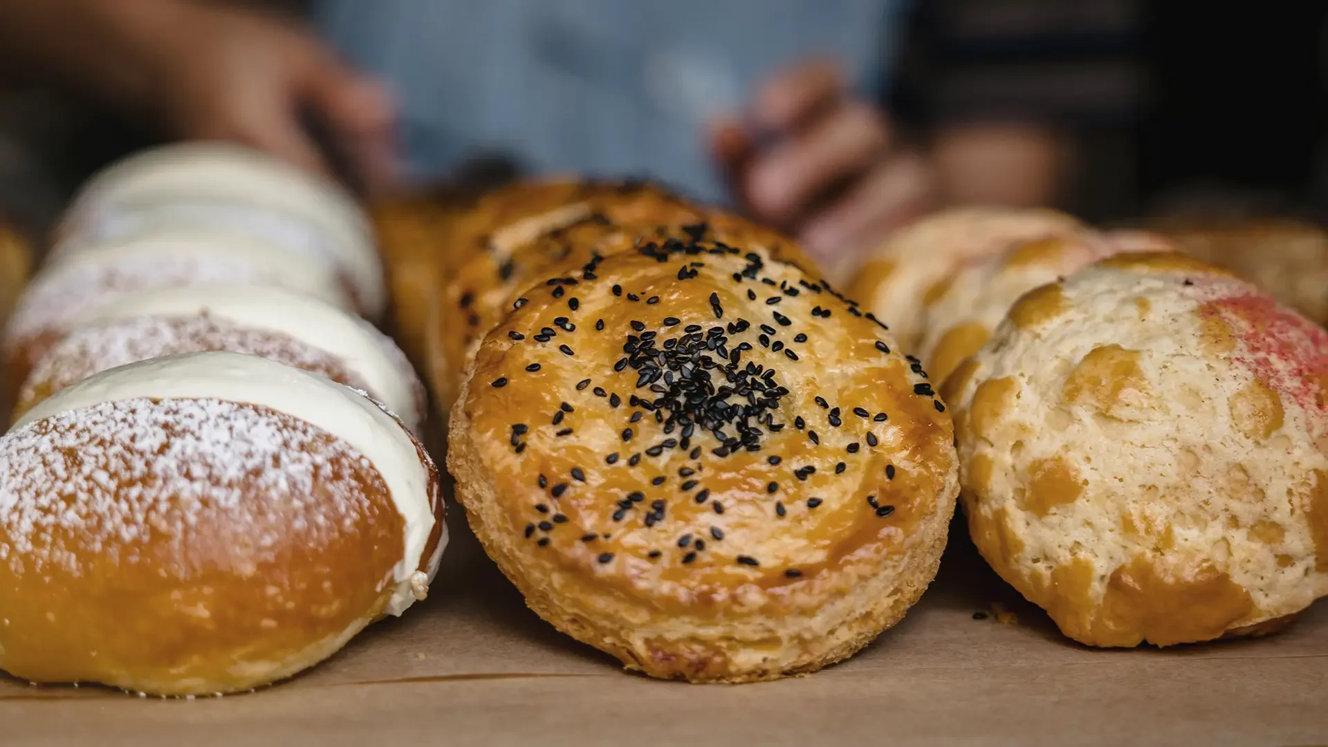 Close-up of assorted baked goods at Warfield's bakery in Clifton Springs, NY, including pastries topped with sesame seeds, powdered sugar, and icing, arranged on a tray.