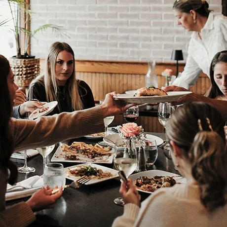 A group of people dining together at Warfield's restaurant in Clifton Springs, NY, with a server serving food at the table.