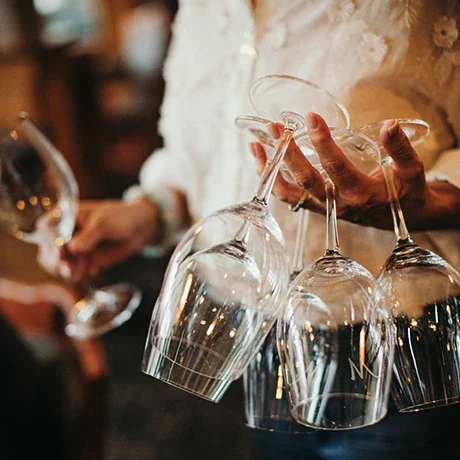 A person holding a wine glass, with several other wine glasses hanging upside down from a tray or rack, at a social gathering or restaurant.