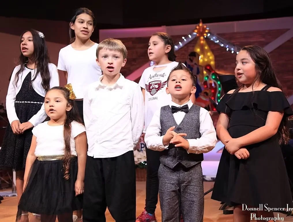 Children performing in a holiday concert on stage with festive Christmas decorations in the background.
