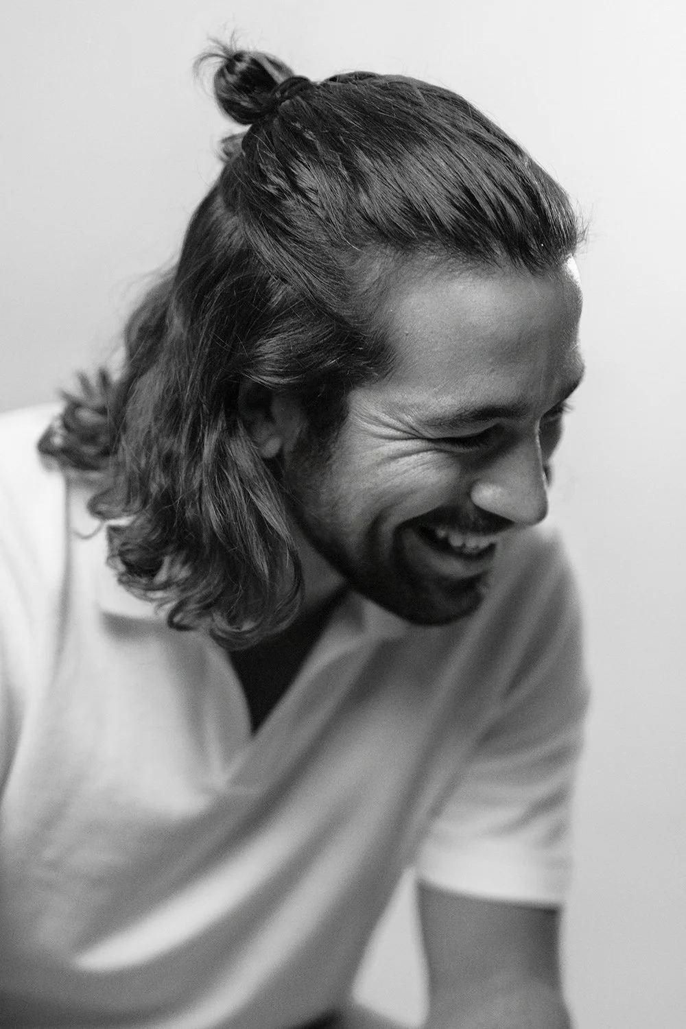 Lächelnder Mann mit längeren Haaren, die an einer Seite hochgebunden sind, in Schwarz-Weiß-Fotografie