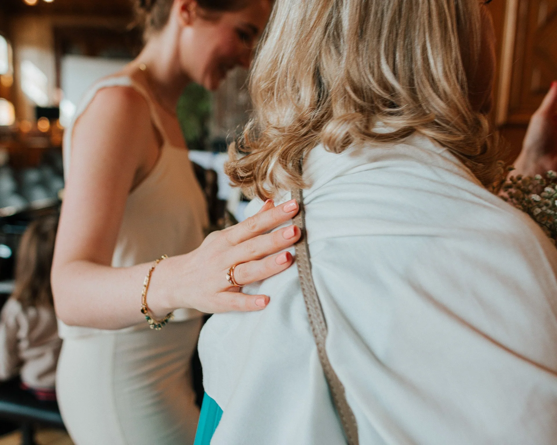 Deux femmes dans une cuisine, l'une avec une robe beige, l'autre avec une veste blanche, partageant un moment chaleureux.