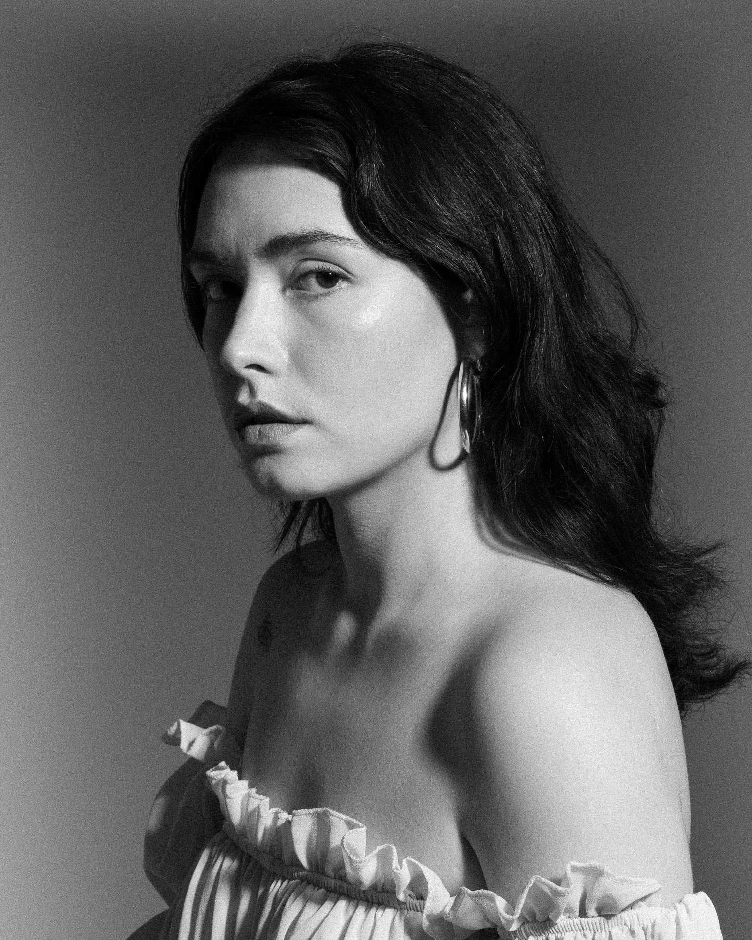 Portrait en noir et blanc d'une femme avec des cheveux longs et ondulés, portant une robe à rayures avec des volants blancs et une boucle d'oreille en boucle.