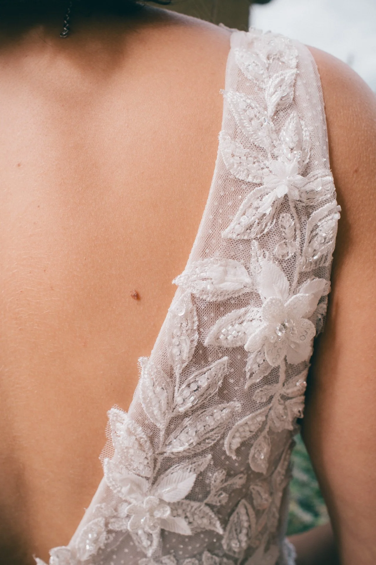 Une personne portant une robe de mariée avec des broderies florales en relief sur le dos, vue partielle du haut du corps à l'épaule.