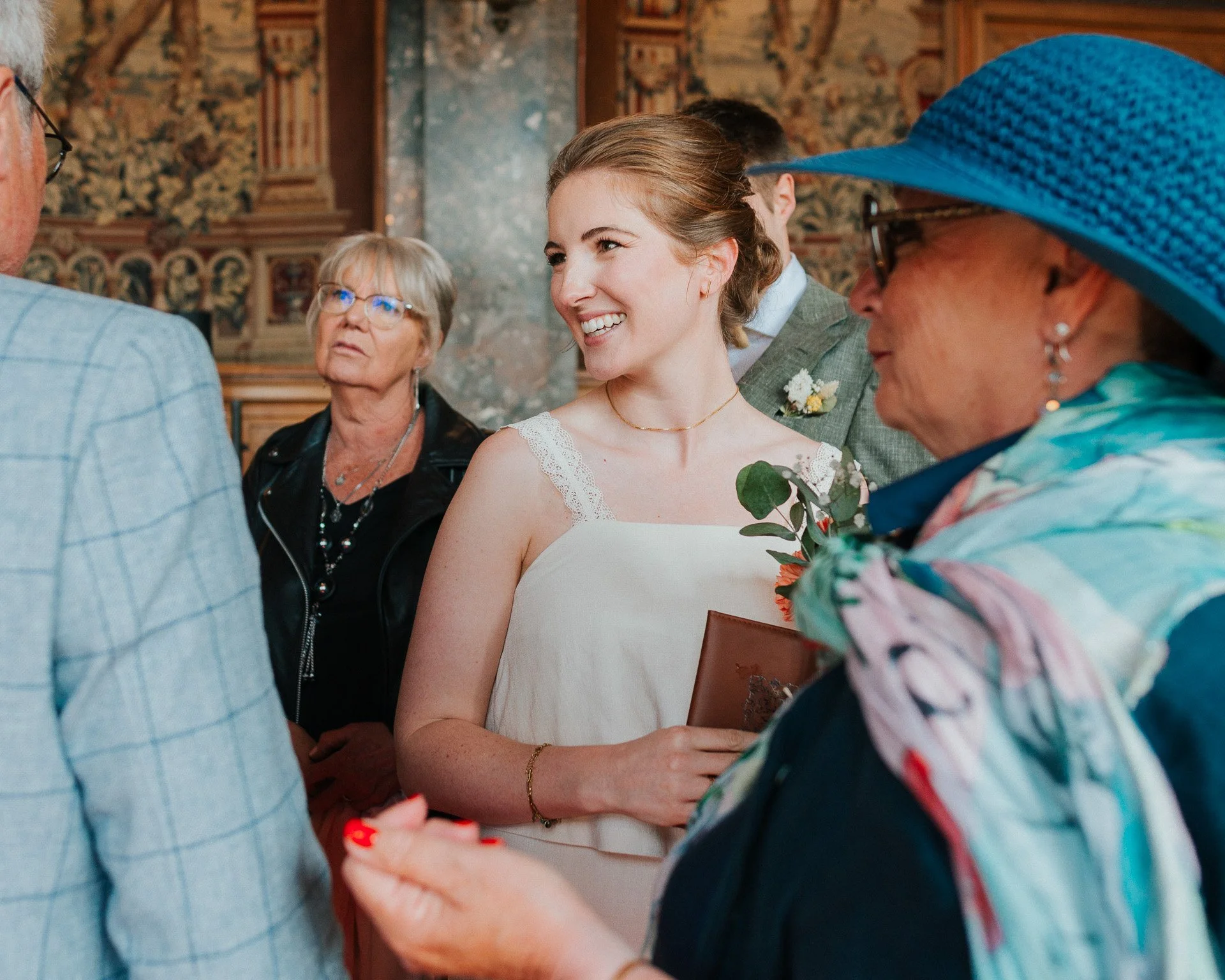 Une mariée souriante entourée de plusieurs personnes lors d'une cérémonie, probablement un mariage dans une église.