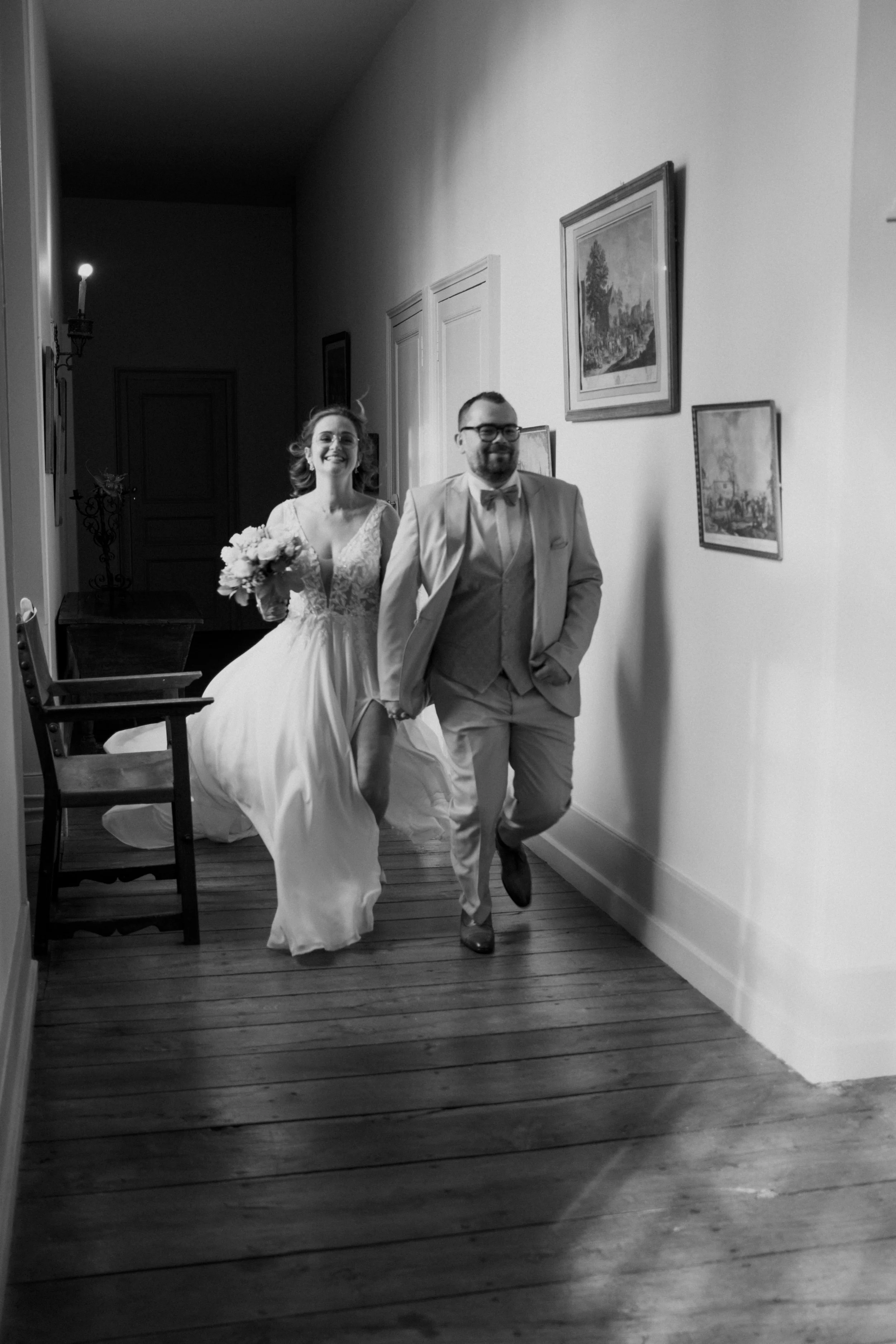 Un couple habillé en costume de mariage marchant dans un couloir intérieur.