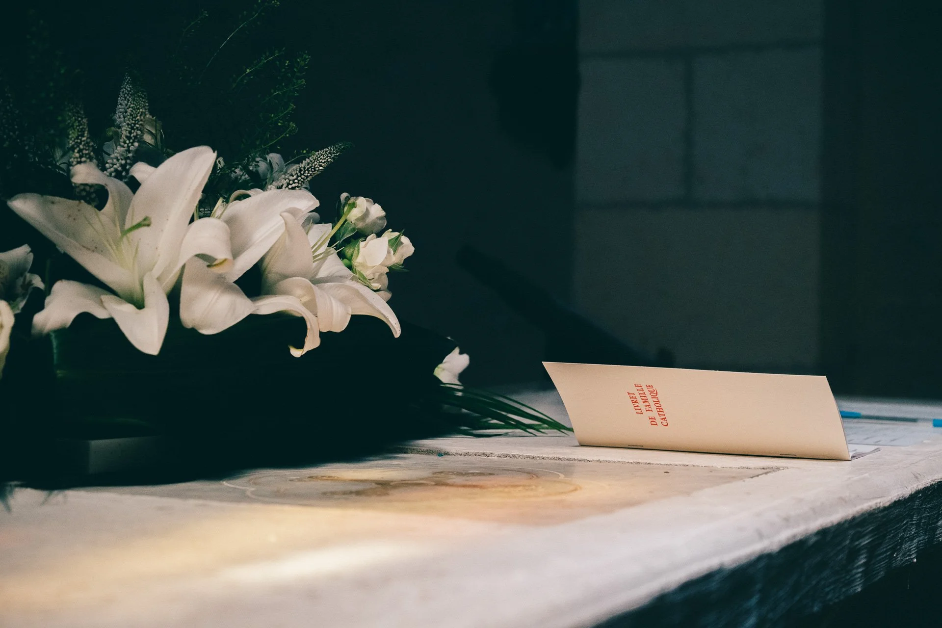 Un bouquet de fleurs blanches avec un message sur une carte pliée posée sur une surface en pierre sombre.