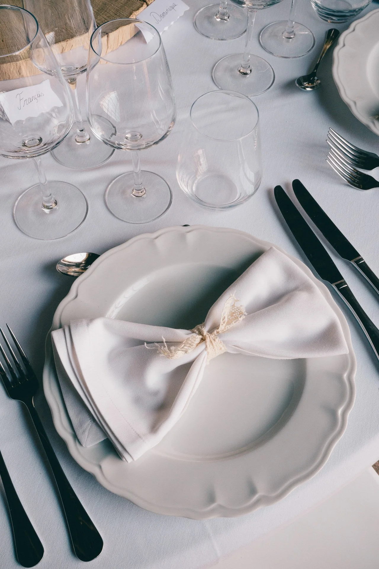 Table élégante avec vaisselle blanche, verres à vin, fourchettes, couteaux et une nappe blanche. Assiette avec un set de serviette blanc enroulé et attaché avec un ruban.
