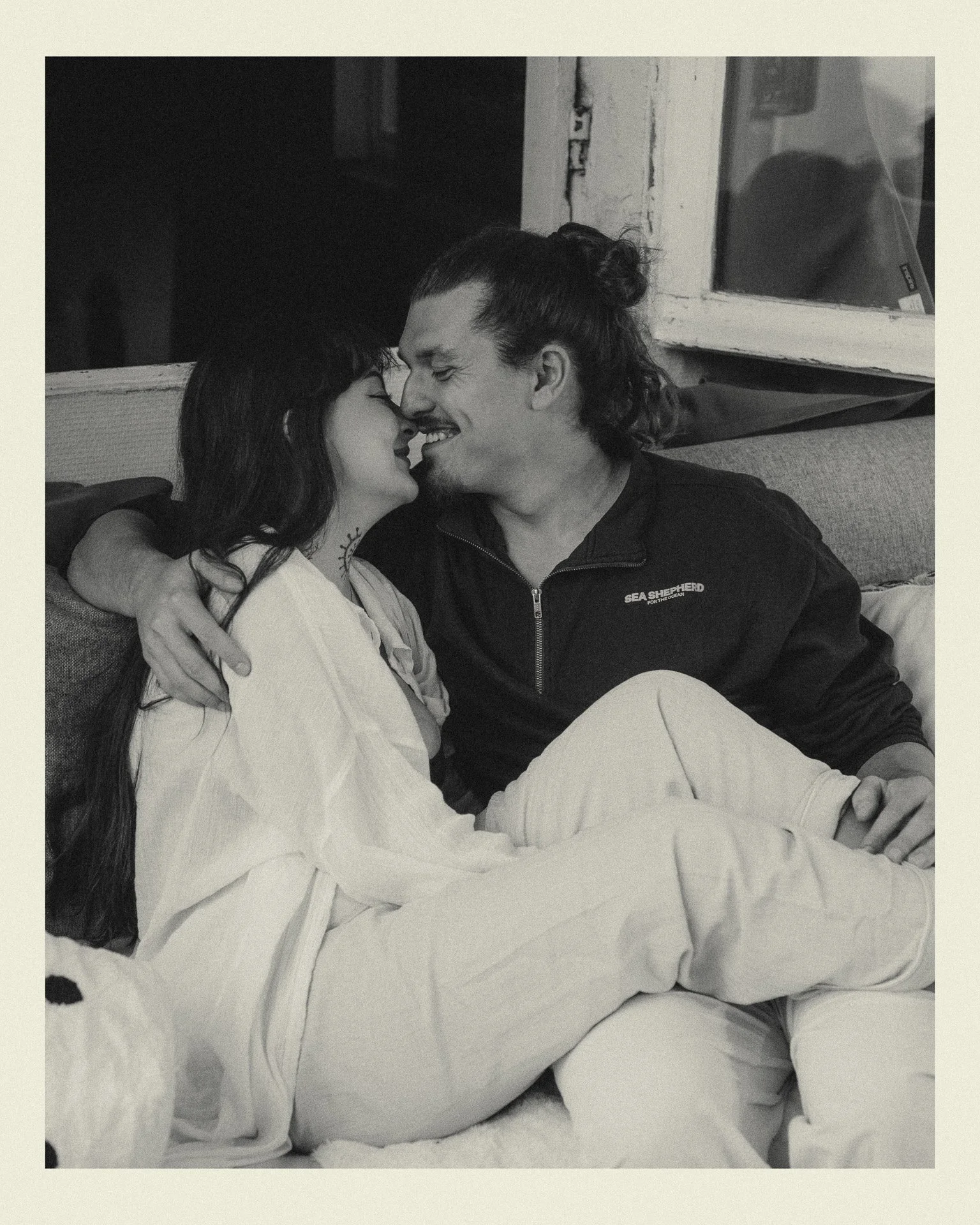 Un homme et une femme, assis ensemble sur un canapé, se regardent avec tendresse, semblent partager un moment intime et affectueux.