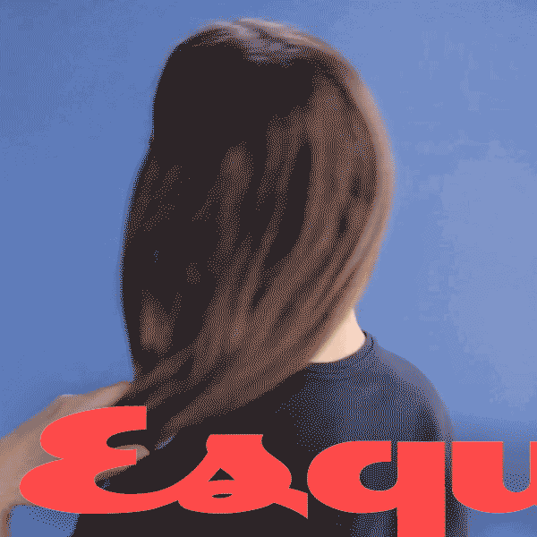 A woman with long brown hair facing away against a blue background, holding a large red object with black and white text.