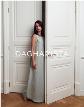 A woman in a long gray dress standing behind an open white door in a room with wood flooring.