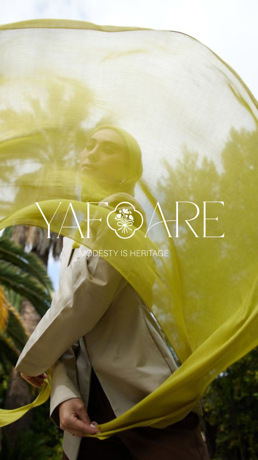A woman holding a large, yellow, semi-transparent umbrella outdoors with trees and sky reflected on it. The umbrella has text that reads 'YAFARE' and 'MODESTY IS HERITAGE' with a logo of a tree inside a decorative border.