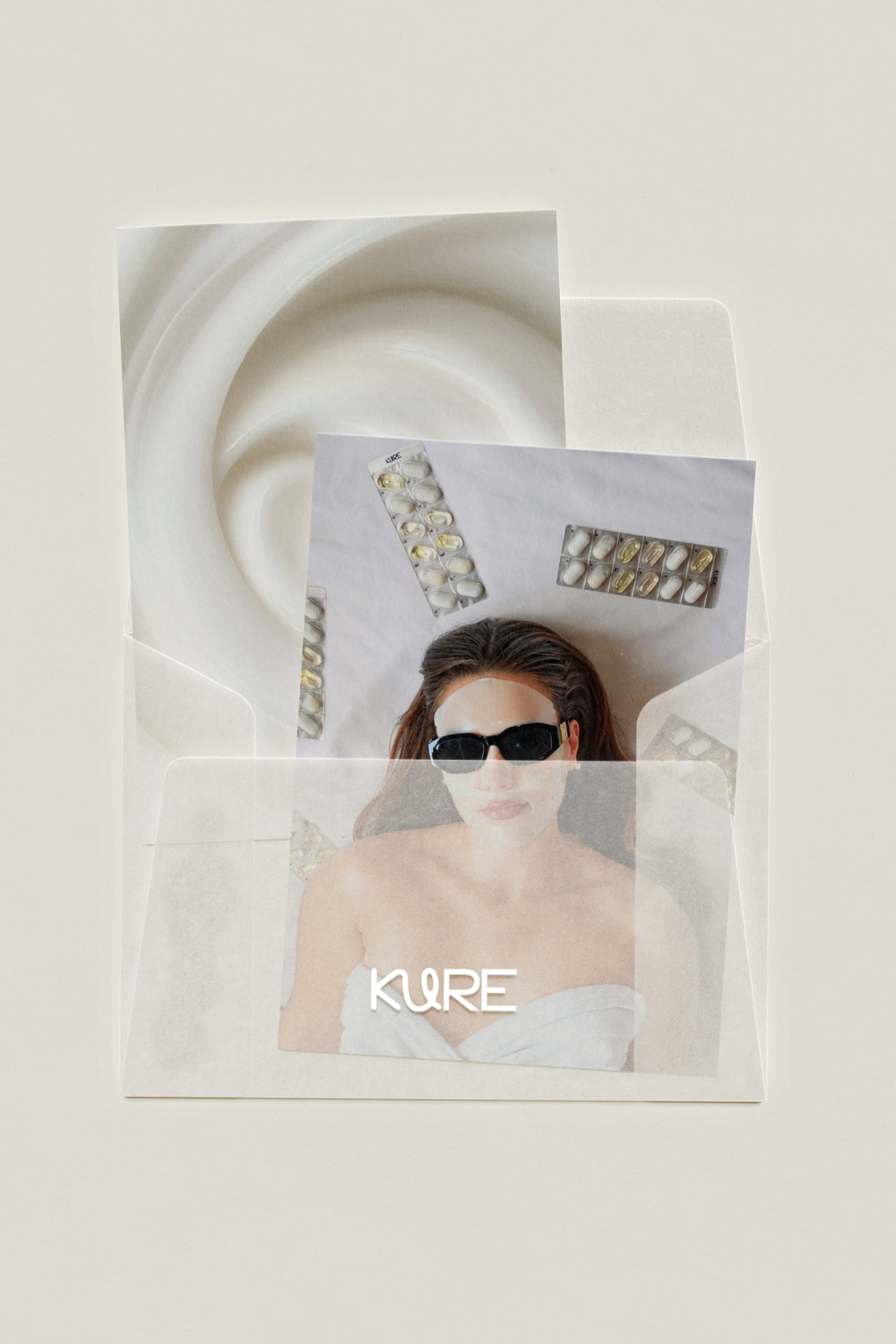A woman wearing sunglasses and a towel wrapped around her chest is enclosed in a transparent plastic sheet with the word 'KORE' printed on it. Behind her, there are multiple blister packs of capsules attached to a ceiling or wall, creating a pattern.