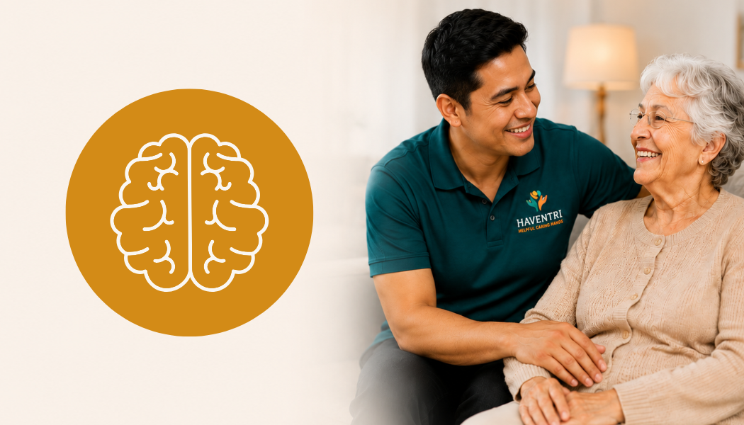 A smiling young man in a teal shirt with the logo 'Haventri' sitting next to an elderly woman with white hair and glasses, both smiling and engaging in a warm, friendly conversation indoors.