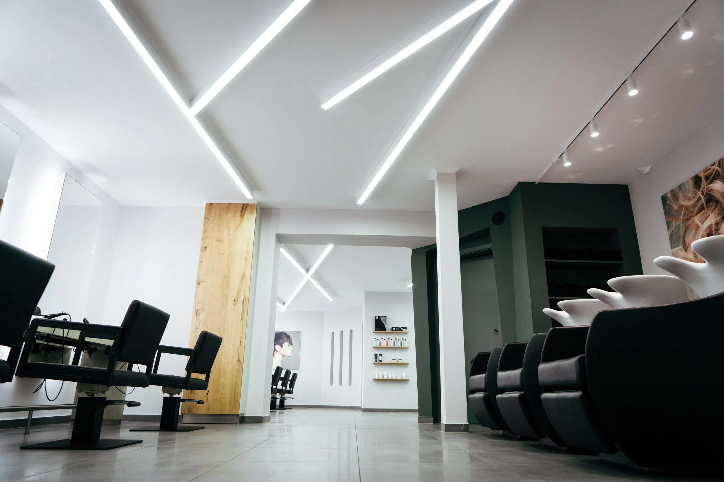 Innenraum eines modernen Friseursalons mit schwarzen Sitzen, weißen Wänden, und einem Regal mit Haarpflegeprodukten.