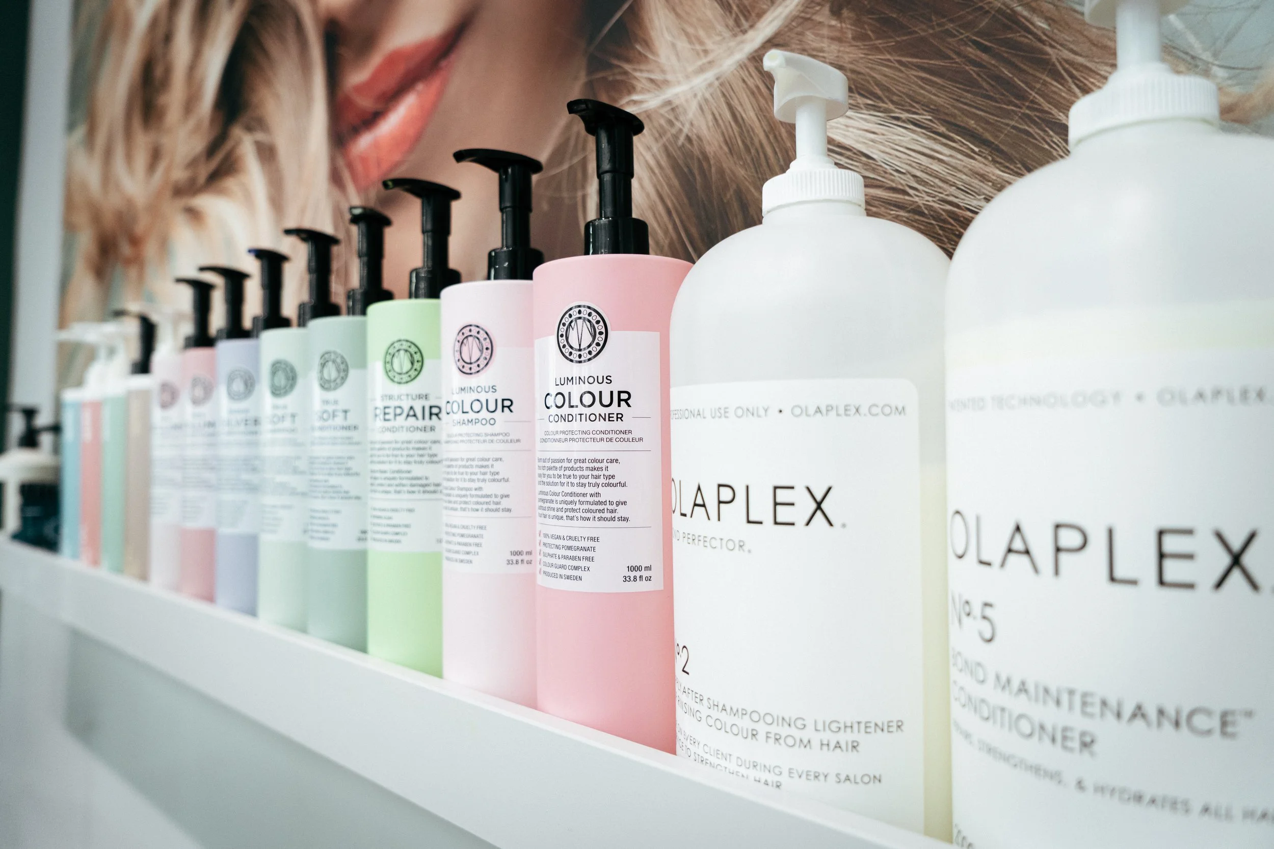Verschiedene Flaschen mit Haarpflegeprodukten wie Shampoo und Conditioner, auf einem Regal.