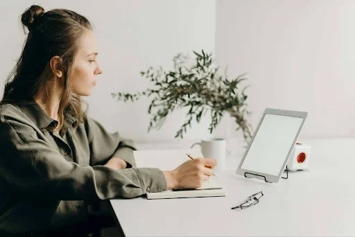 A woman sits at a desk with a laptop and pen, contemplating her career change with focused determination.