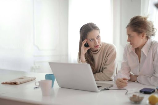 Two women at a table with a laptop, discussing strategies for their career change and future opportunities.