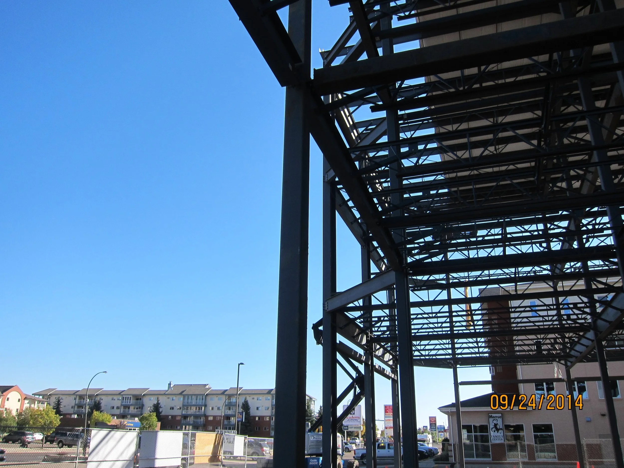 View of construction scaffolding next to a parking lot and a residential apartment building under a clear blue sky.