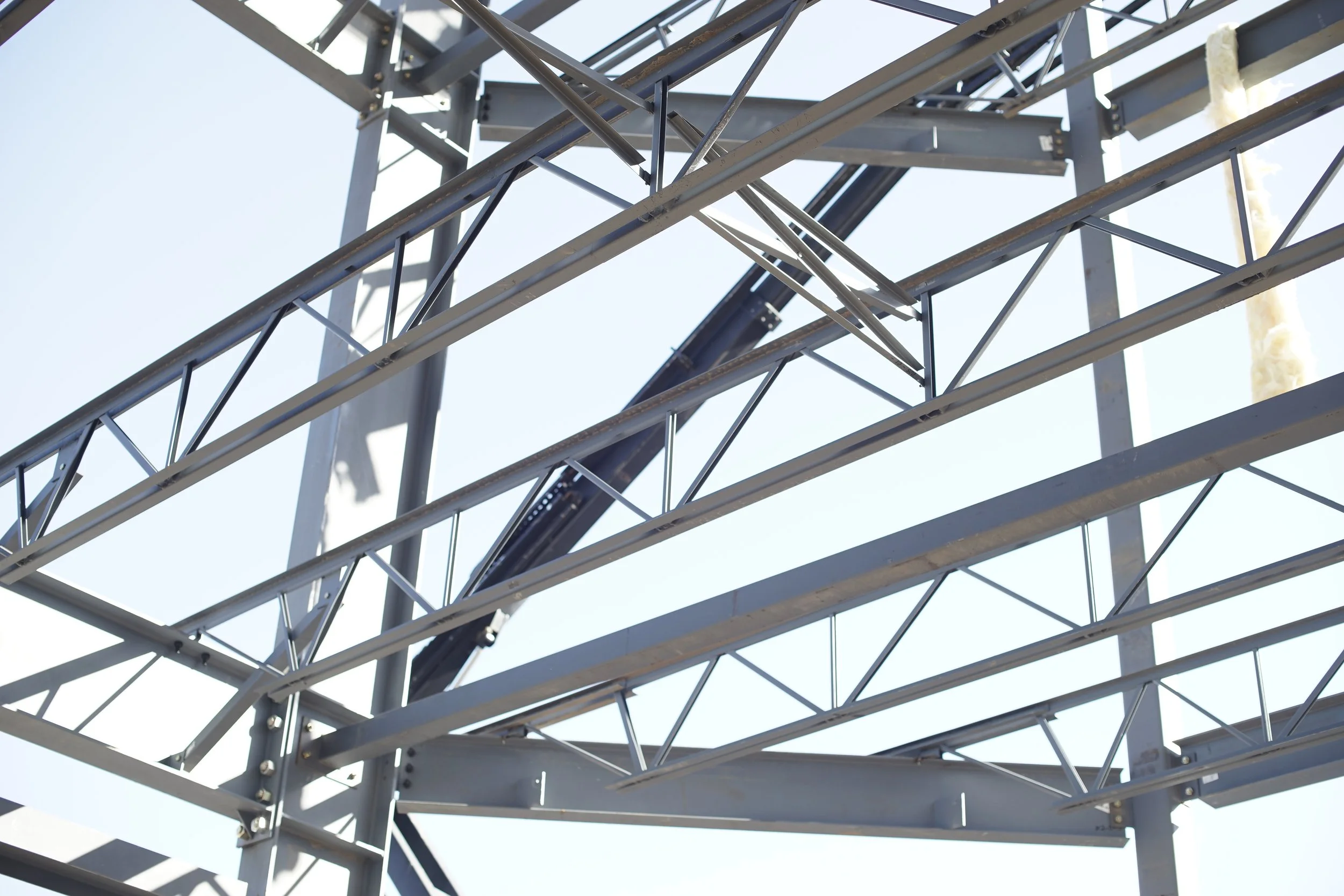 Steel framework of a modern architectural structure, viewed from below against a bright sky.