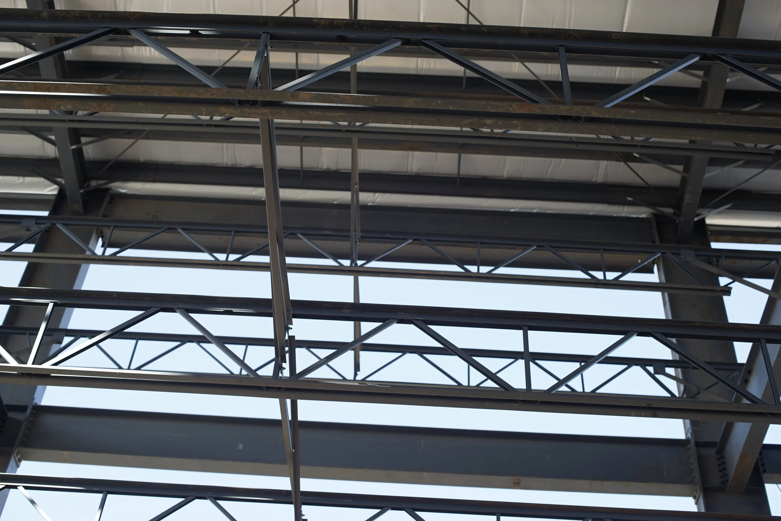 Low-angle view of steel framework of a building with beams and support structures, partially assembled under a metal roof.