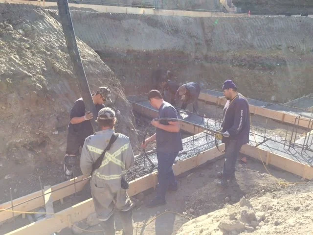 Construction workers pouring concrete into wooden molding on a construction site.