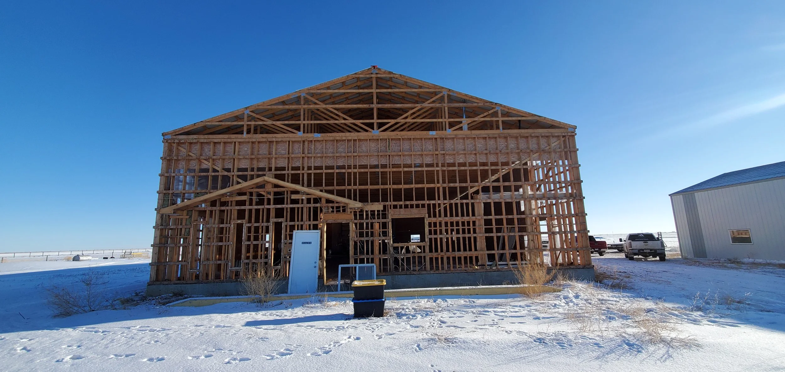 Wooden house under construction with snow on the ground and a clear blue sky.