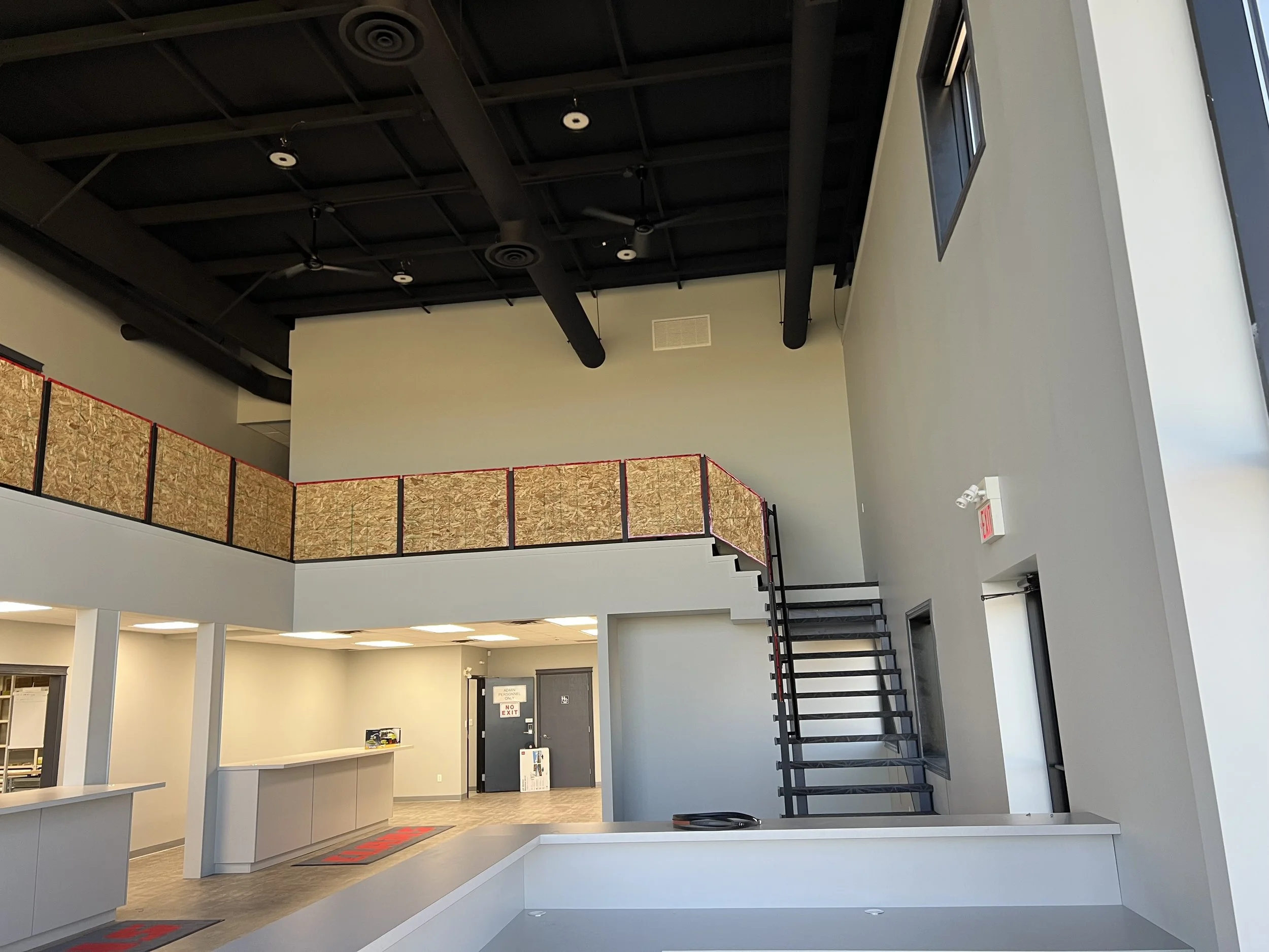 Interior of an empty commercial space with high ceilings, a staircase, and a reception area.