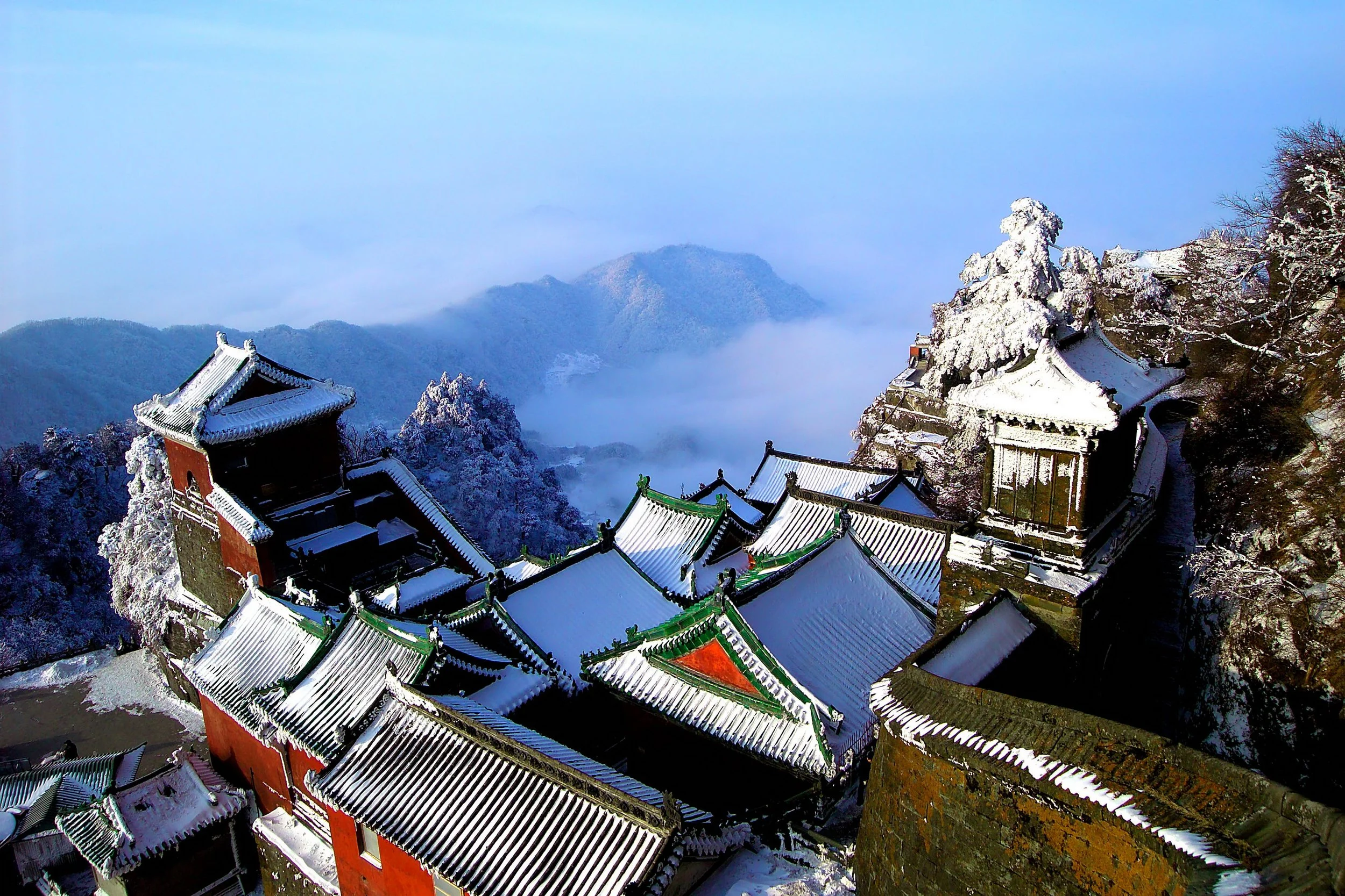 Snow-covered Wudang Mountain temple rooftops rising through the clouds in winter