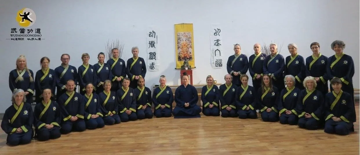 Wudang Gong Dao members kneeling in formation beneath the school banner and calligraphy scrolls