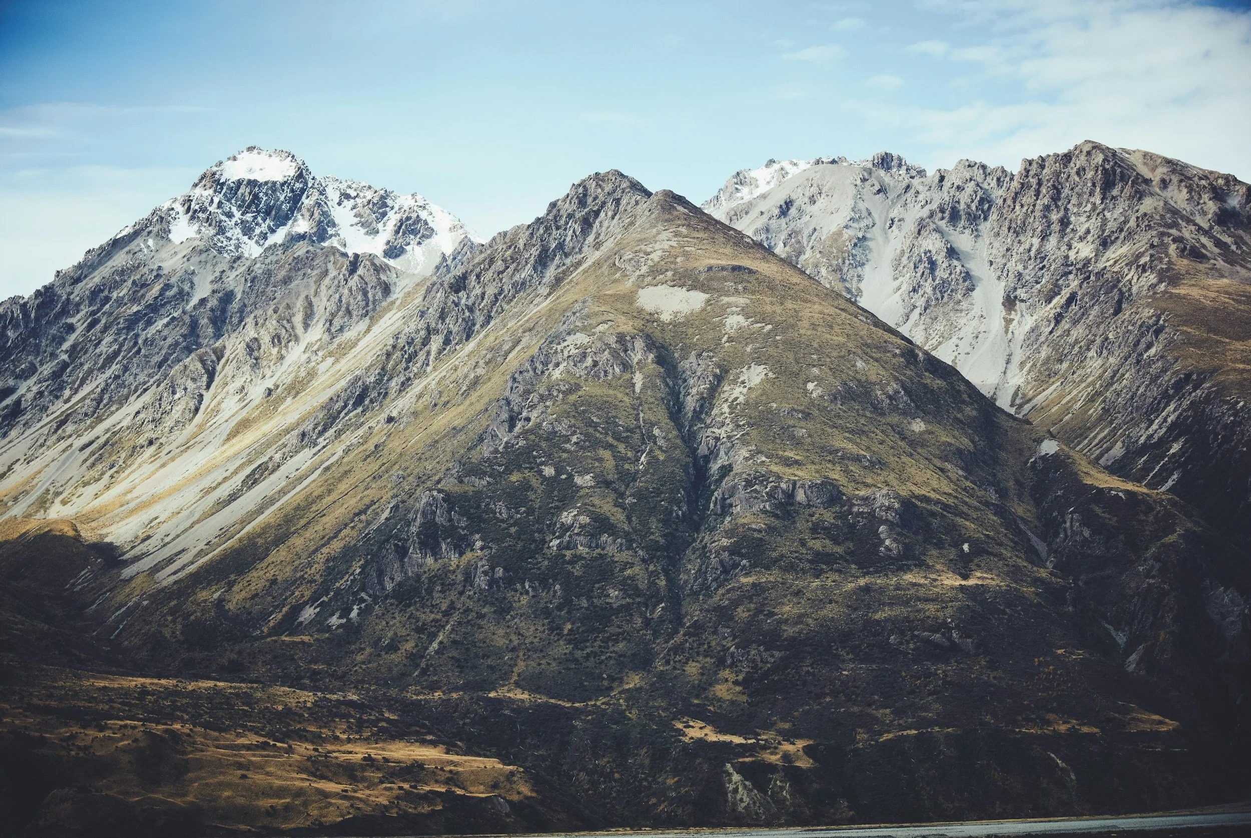 Mountain range with snow-capped peaks and grassy slopes under a cloudy sky.