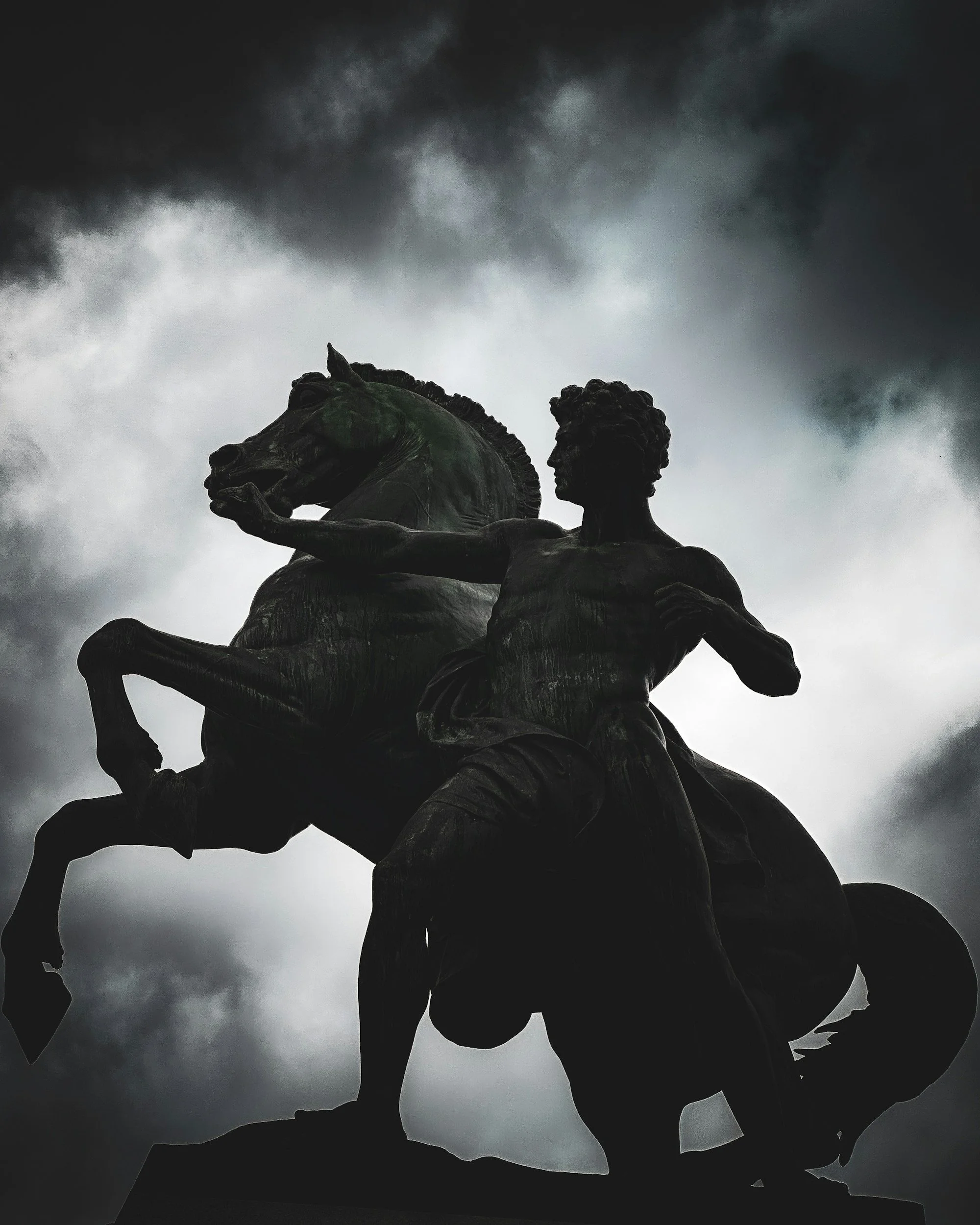 A bronze statue of a man on a horse against a dark, cloudy sky.