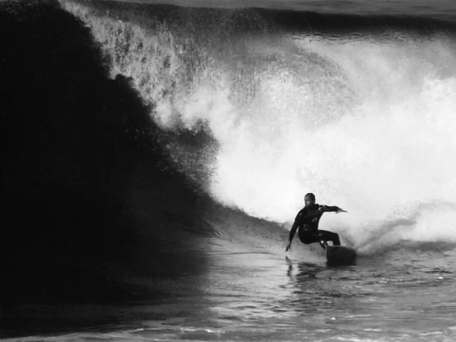 A person surfing on a wave in black and white.