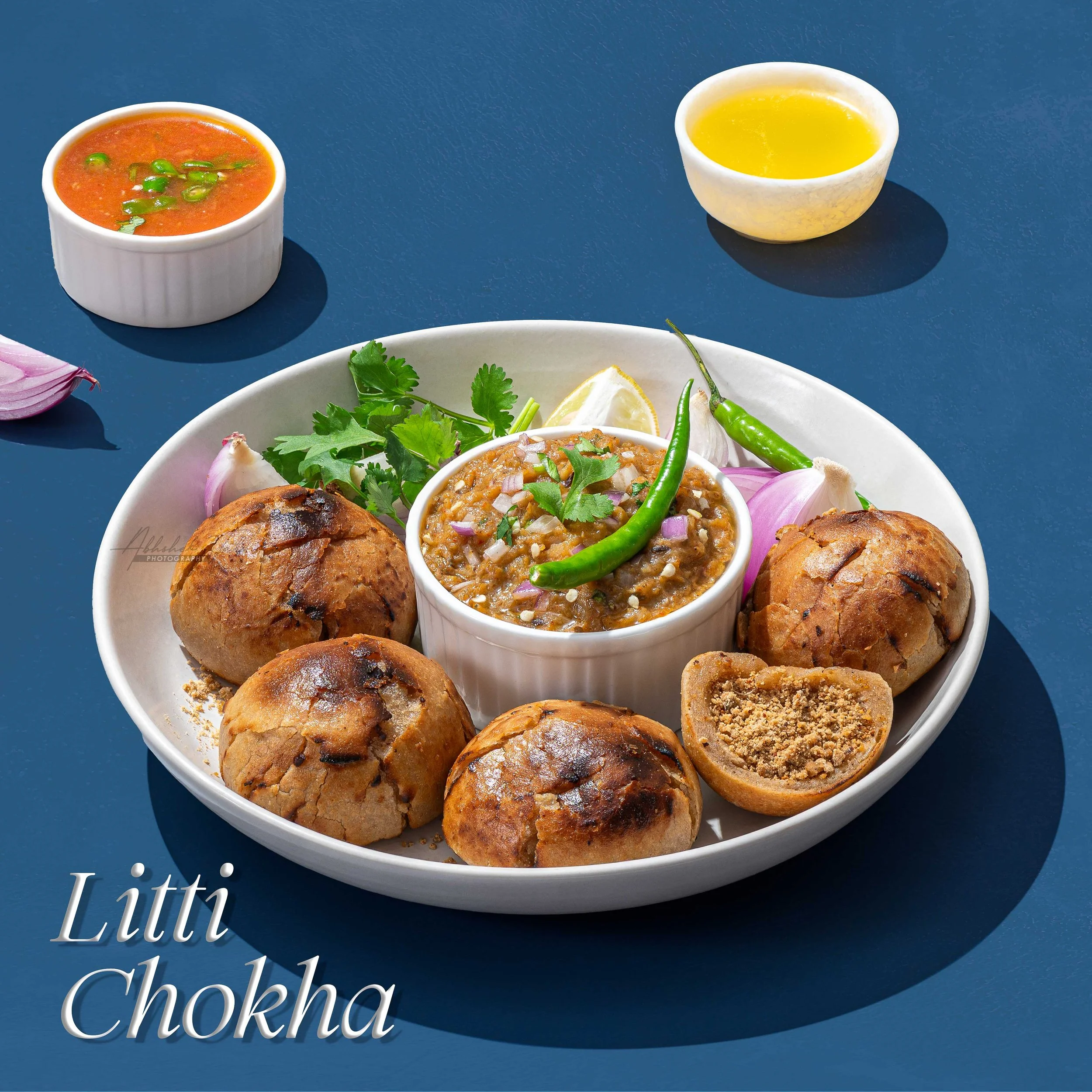 A bowl of Indian chutney, a bowl of yellow sauce, and a plate of savory snacks garnished with cilantro and sliced onions on a blue table.