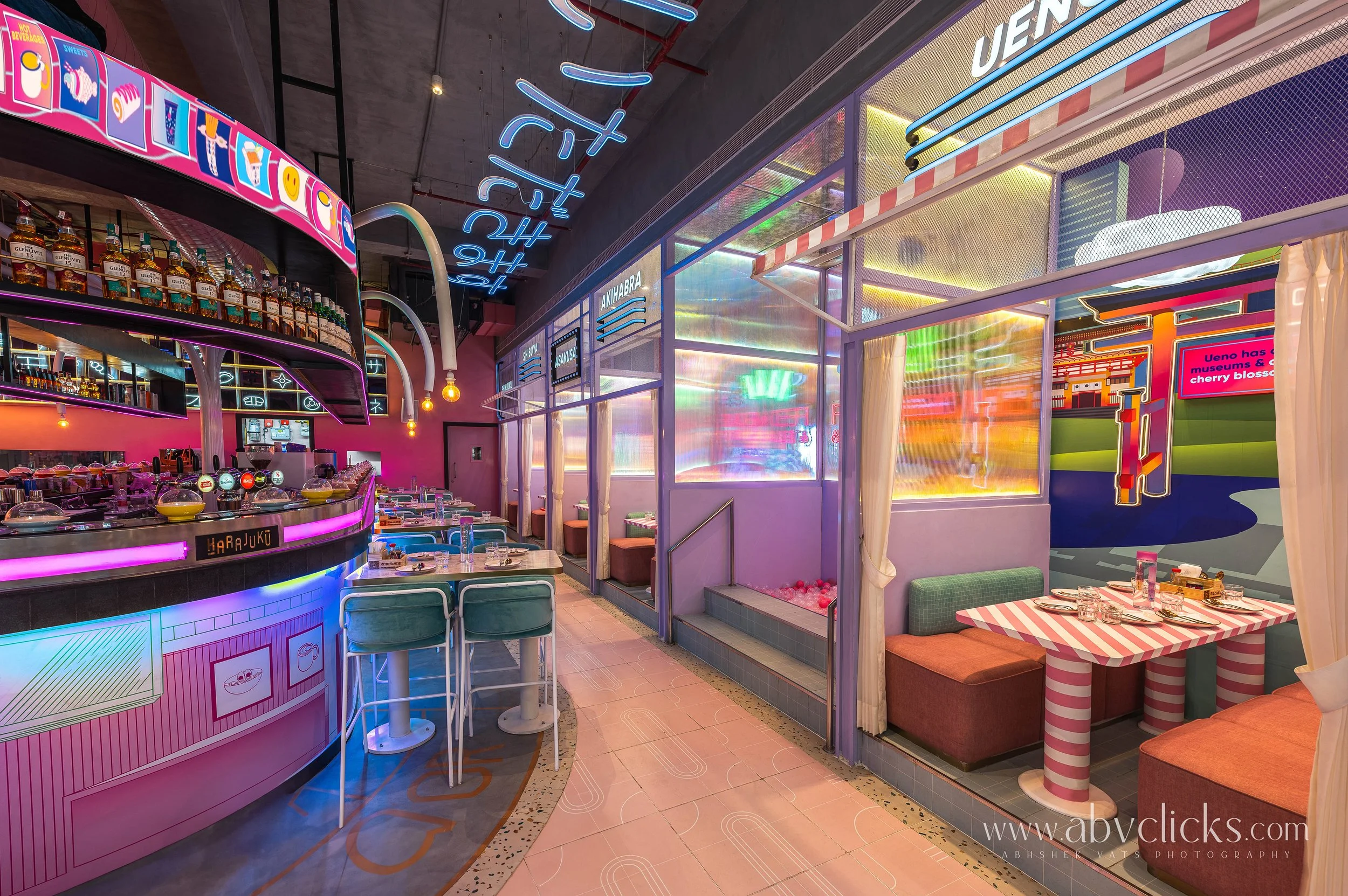 Colorful interior of a modern restaurant or cafe with neon signs, vibrant lighting, and playful decor, featuring seating areas and a bar with bottles.