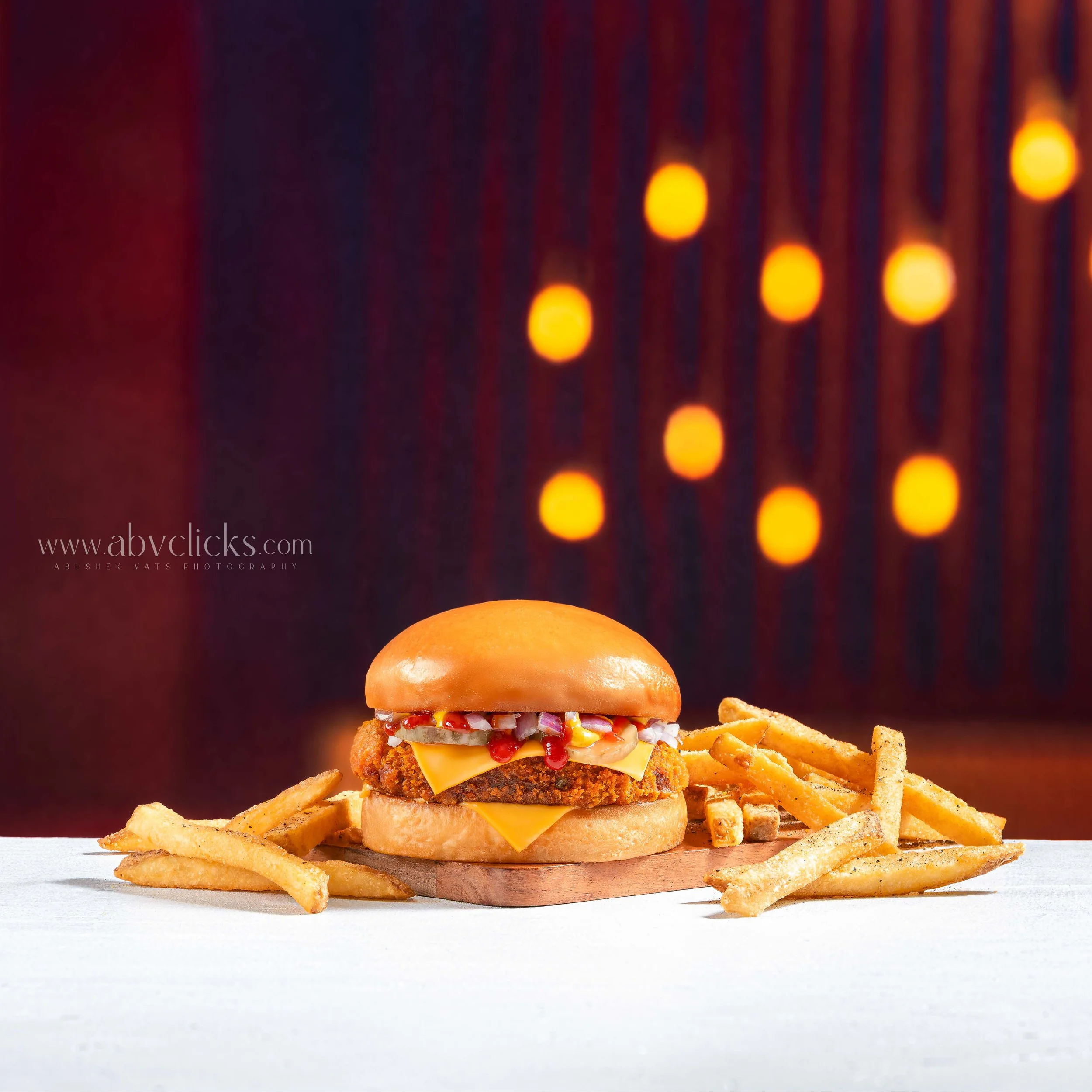 A crispy chicken sandwich with lettuce, tomato, cheese, and sauce, served on a bun, surrounded by crispy french fries against a dark background with warm lighting.