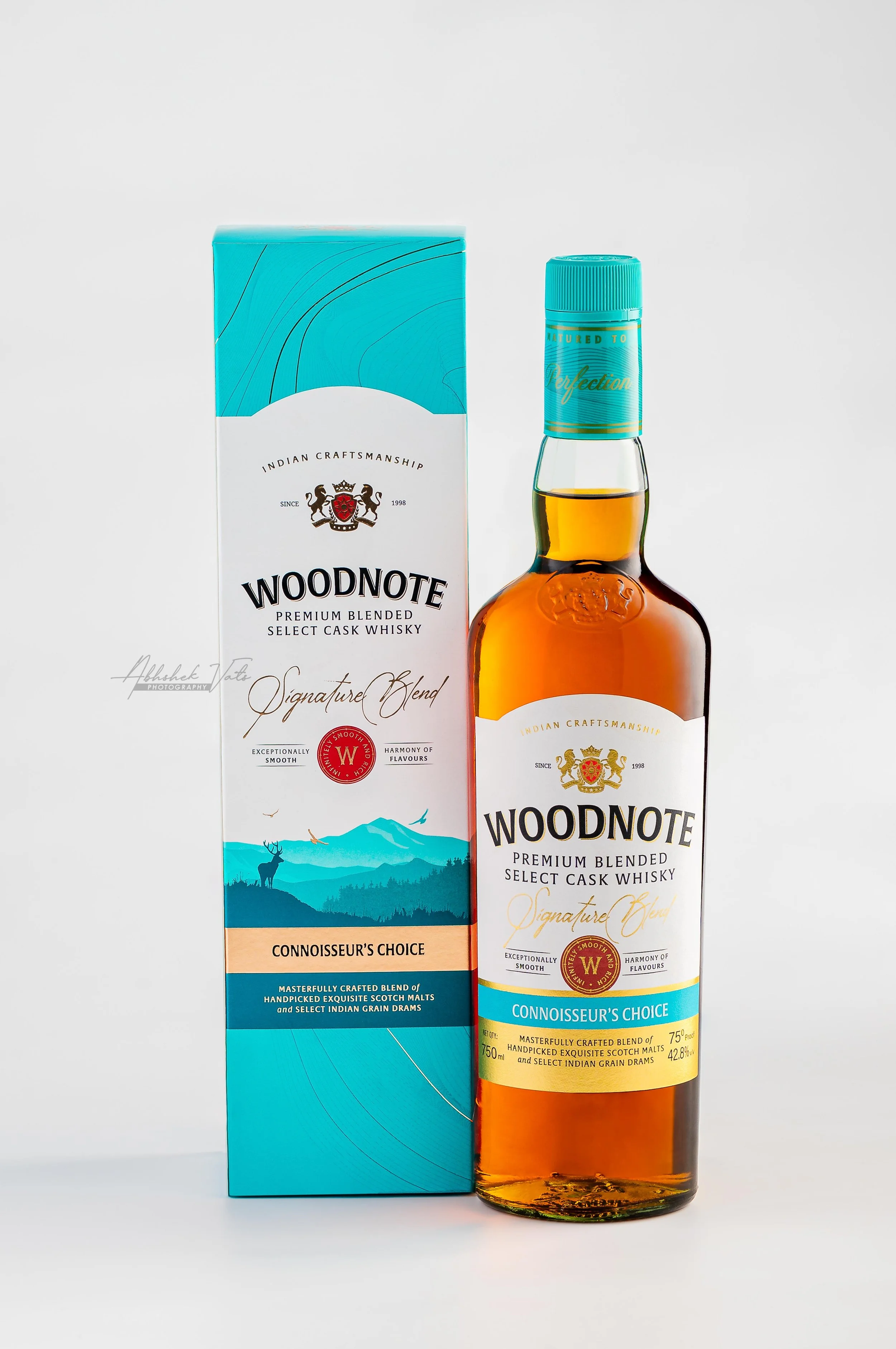 Bottle of Woodnote premium blended whisky next to its blue packaging box with mountain and deer illustration.