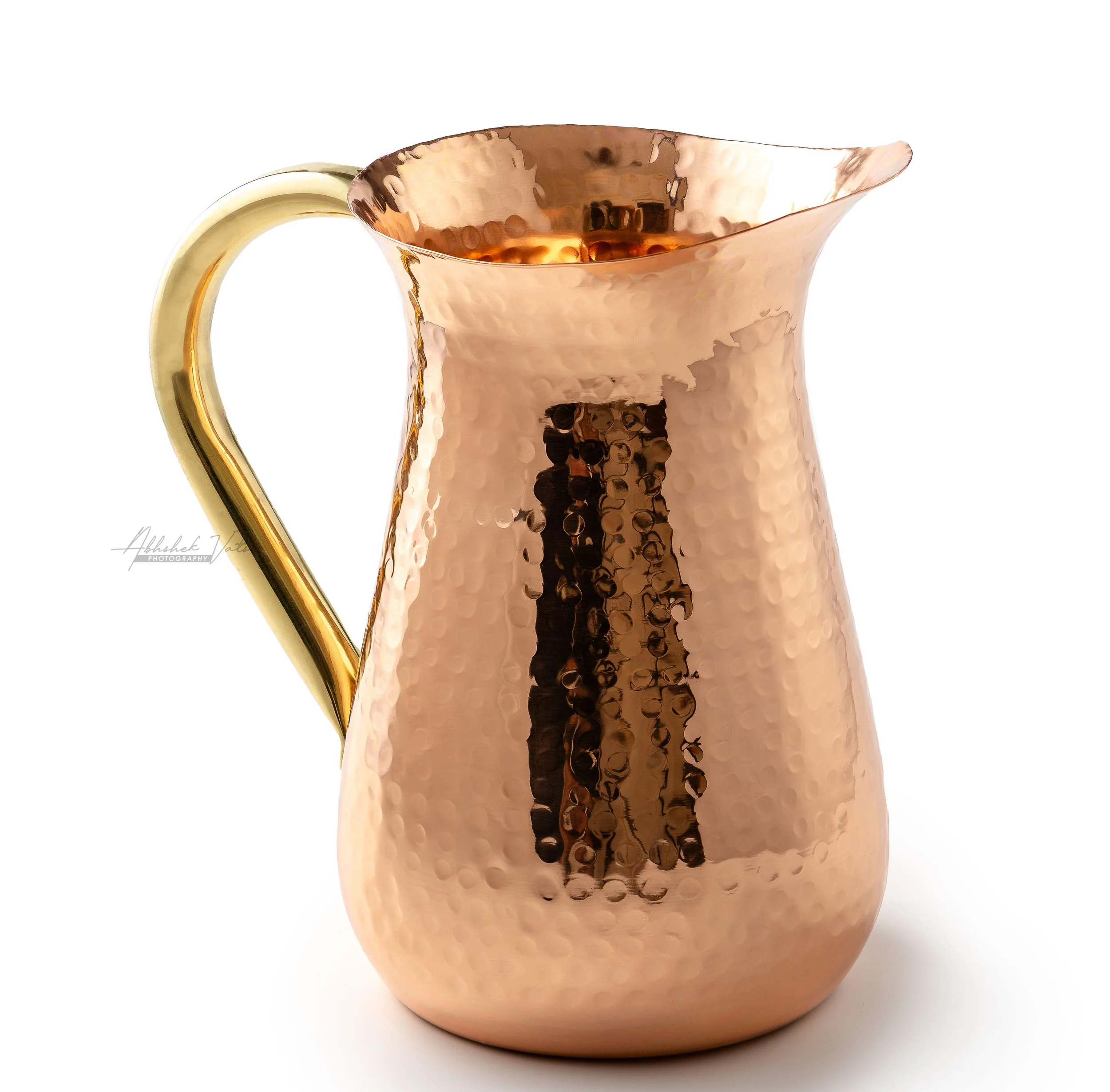 A shiny, hammered rose gold pitcher with a handle and spout, empty inside, placed against a plain white background.