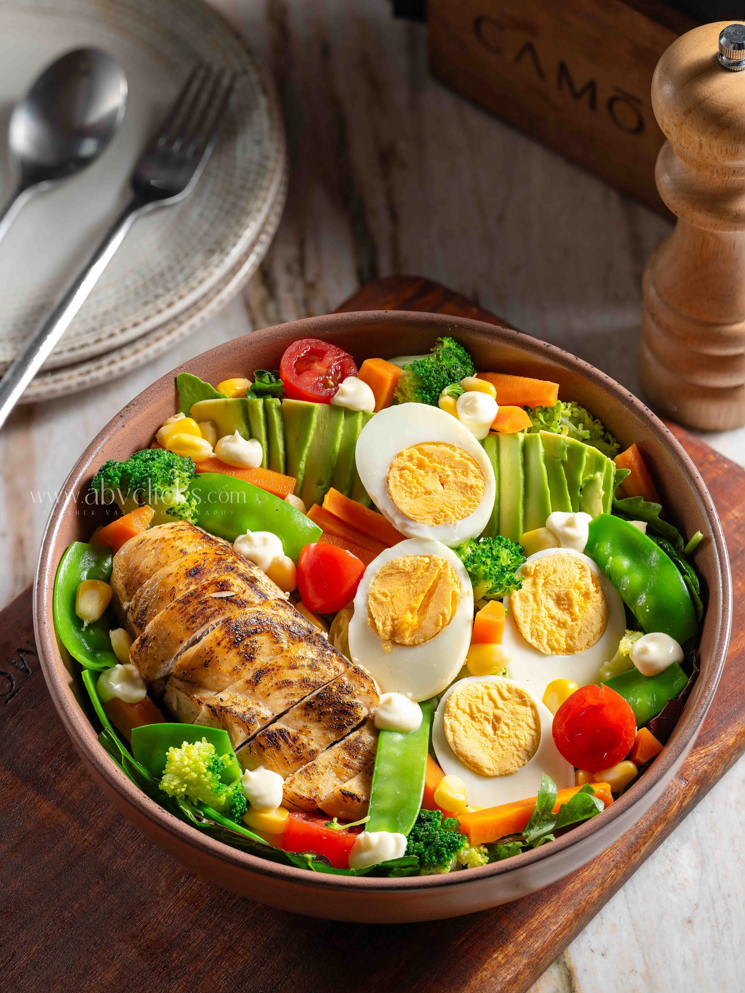 Vegetable salad with boiled eggs, cherry tomatoes, broccoli, carrots, sugar peas, corn, and grilled chicken in a bowl.