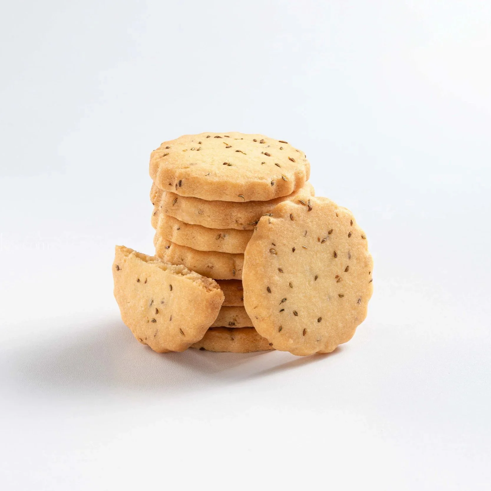 A stack of five round, golden-brown cookies with small dark specks, with one cookie broken in half, set against a plain white background.