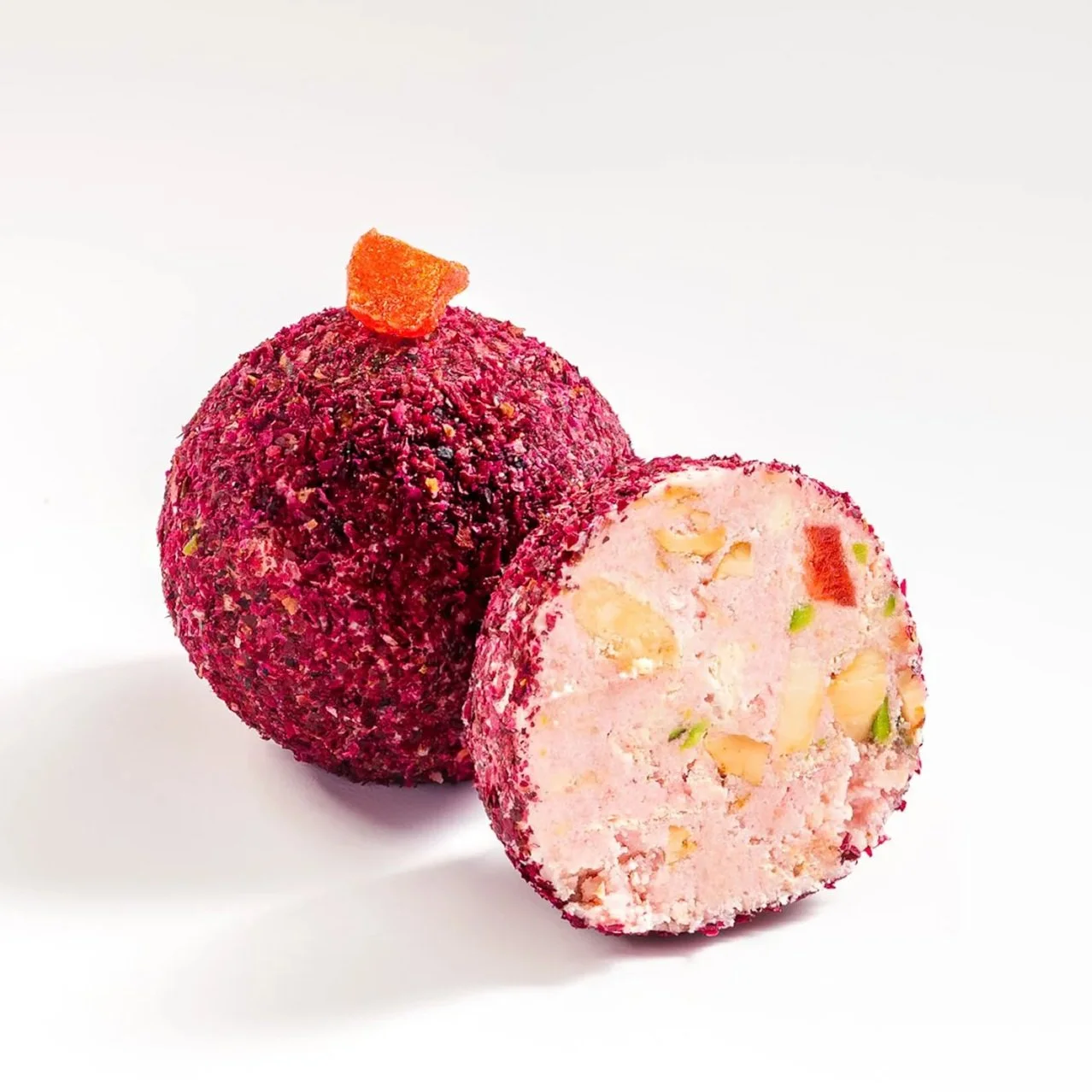 Two pink ice cream truffles coated with pink sprinkles, one whole with an orange piece on top, and one cut in half revealing a creamy interior with nuts and fruit pieces, on a white background.